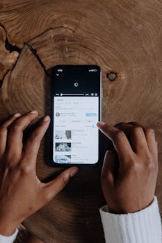 Overhead view of hands browsing videos on a smartphone placed on a wooden background.